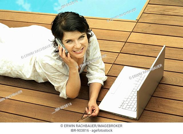 Woman reclined on a wooden terrace with a laptop in front of her, web surfing, online dating, Internet purchases