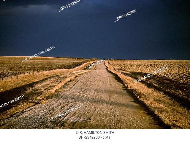 Agriculture - Gravel country road passing through harvested farm fields in Autumn with dark storm clouds above / Iowa, USA