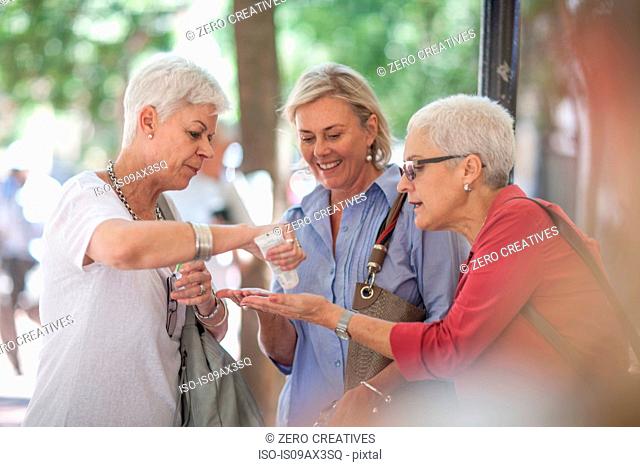 Senior and mature women sharing hand cream in city