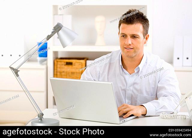 Casual young businessman working at home on laptop compuer, looking at screen