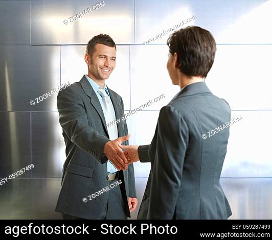 Smiling businessman and businesswoman shaking hands in modern design office