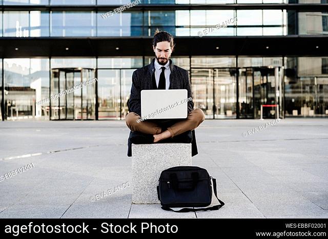Entrepreneur working on laptop while sitting cross-legged on bench