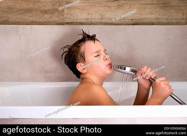 Happy boy holding shower head and singing while washing in bathroom Child bathe at home healthy childhood