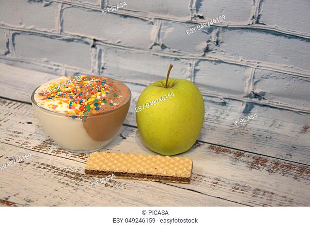 Chocolate and vanilla ice cream with decor, green apple and waffle lie on a wooden table