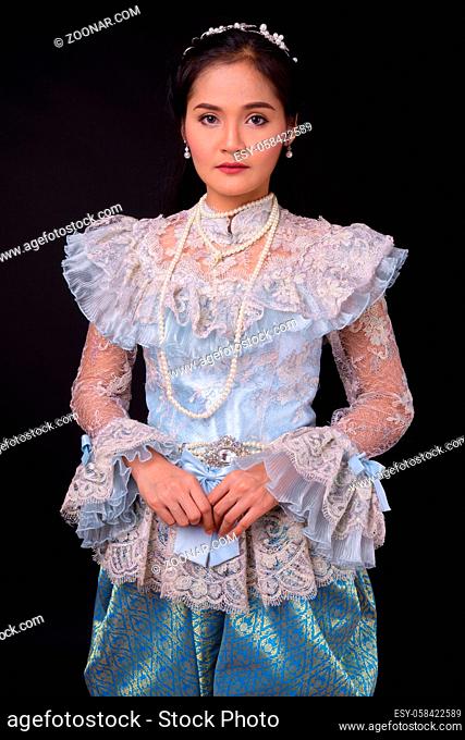 Studio shot of young beautiful Asian woman wearing Thai traditional clothes against black background