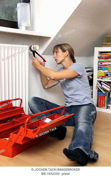 Young woman repairing the thermostat of a radiator