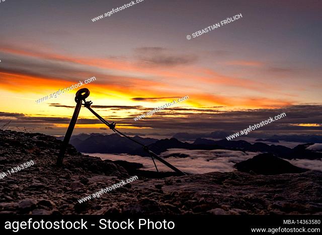 Old wire rope belay on Guffert at sunrise over the Alps. In the background fog over the Rofan and the Brandenberg Alps, with colorful clouds