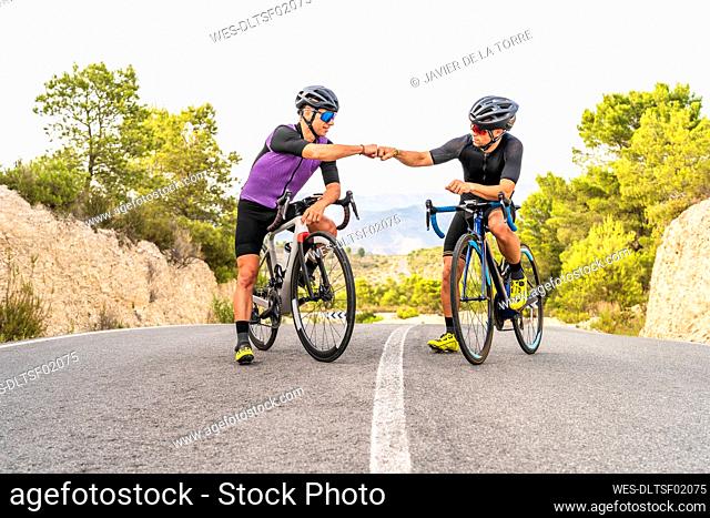 Male athletes doing fist bump while sitting on bicycles
