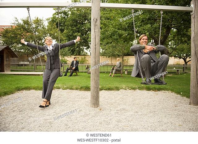Germany, business people sitting on swings in playground