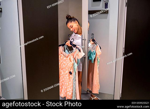 Beautiful girl with lots clothes on the background of a fitting room in a boutique