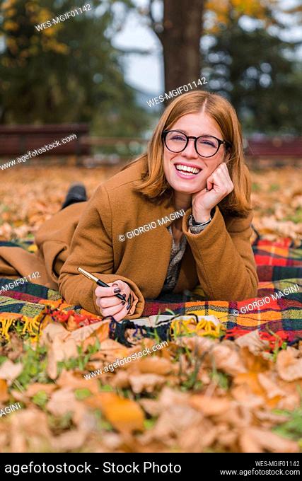 Mujer feliz acostada sobre una manta en el parque de otoño