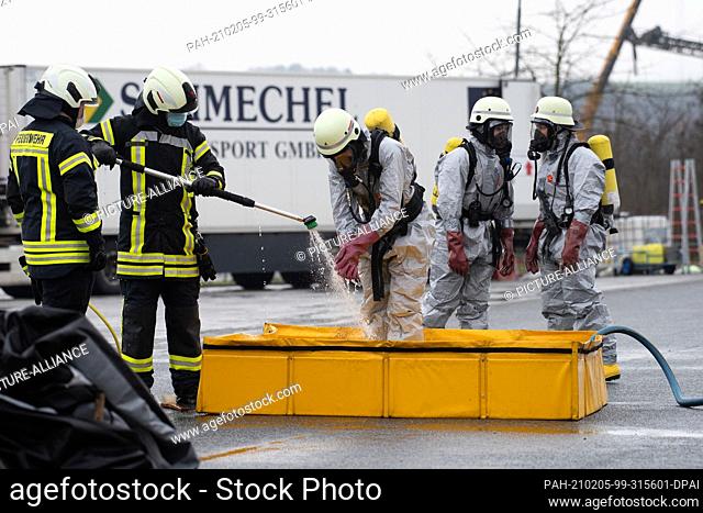 05 February 2021, Lower Saxony, Northeim: Emergency workers in chemical protective suits are decontaminated by firefighters at a car yard