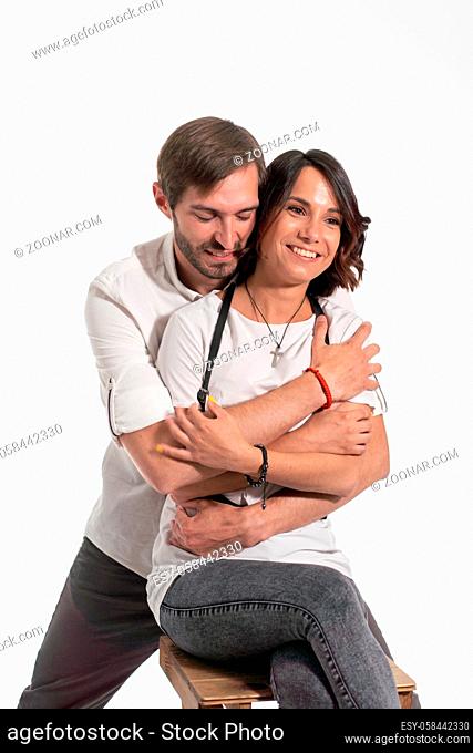 Man hugs woman from behind. Woman sits on chair and smiles. Isolated white background. Presentation of Nanlite Studio LED Lighting. Backstage