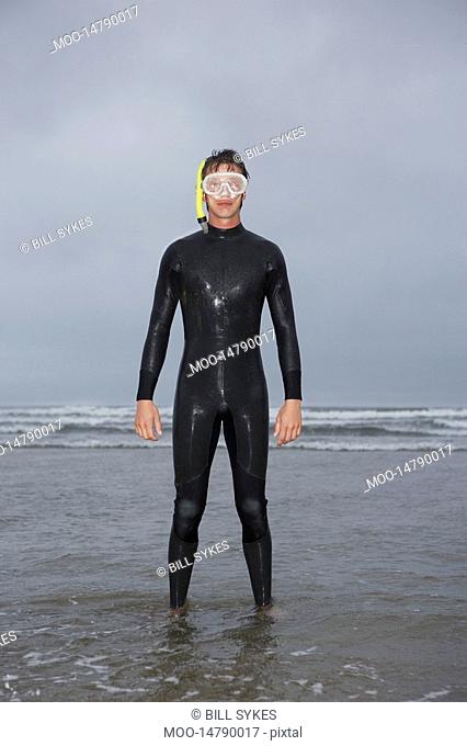 Man in wetsuit wearing snorkle standing in water on beach portrait