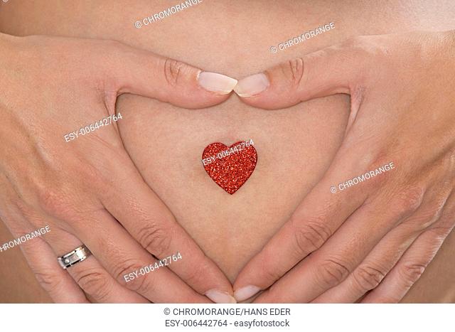 Woman makes on her baby belly with hands a heart