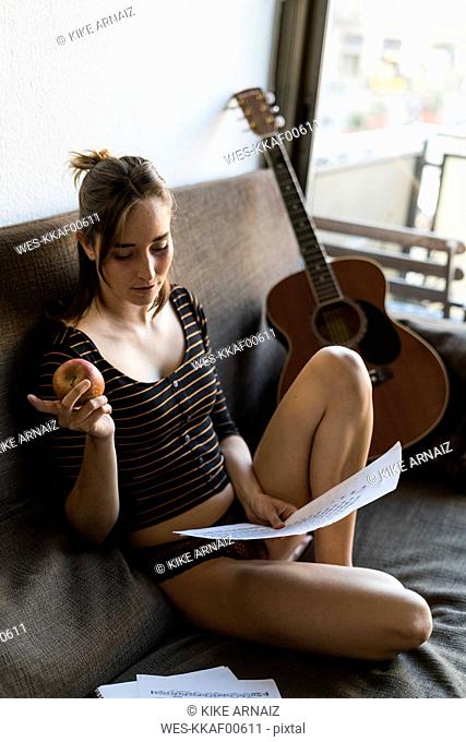 Young woman with music sheets and guitar sitting on couch