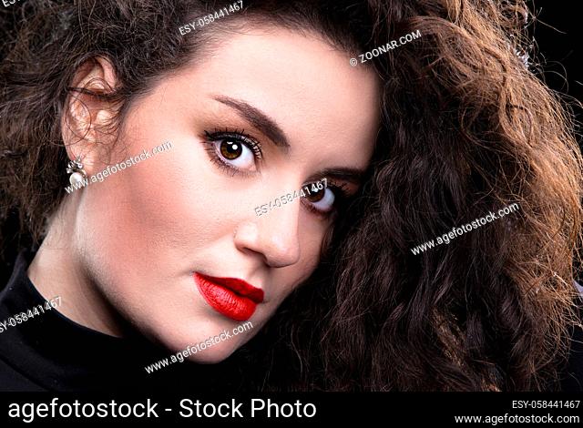 Close-up of a beautiful brunette girl with curly hair and bright makeup on a dark background