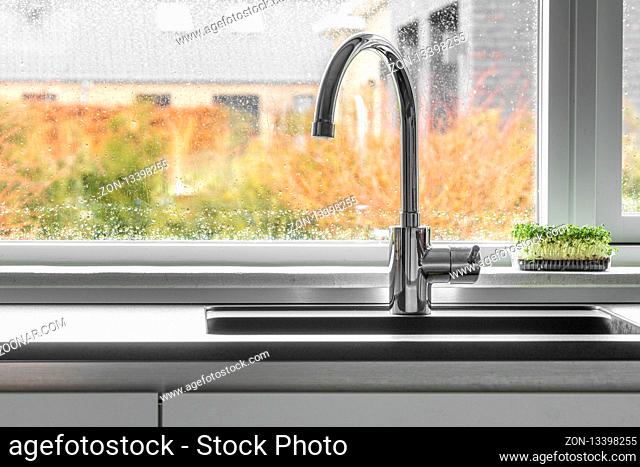Chrome faucet by a kitchen sink with a wet window in the background