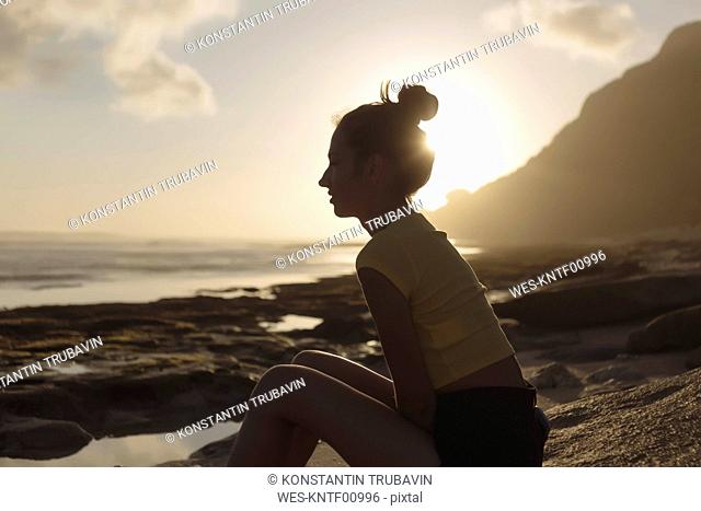 Indonesia, Bali, young woman sitting on the beach at sunset