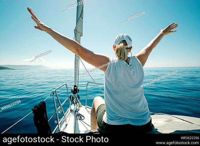 Woman sitting on the ships bow enjoying the yacht trip with arms wide open. Sailing, yachting and travel concept