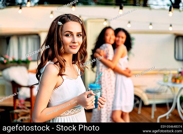 Beautiful young woman portrait during picnic beside her camper van and friends on background. Vacation, trip and holiday concept