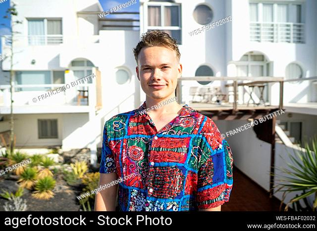 Smiling young man standing in front of house on sunny day