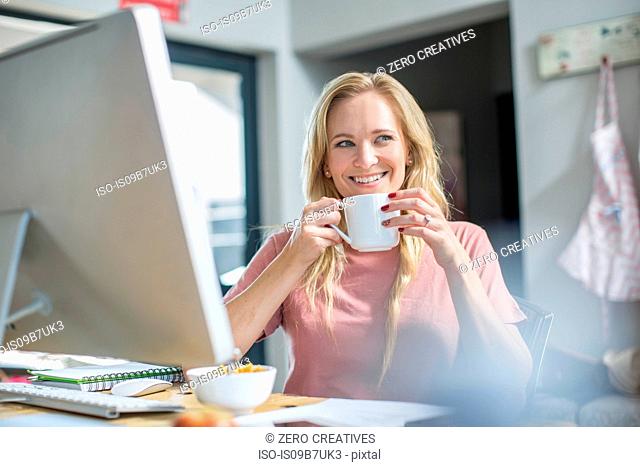 Woman at computer drinking coffee smiling