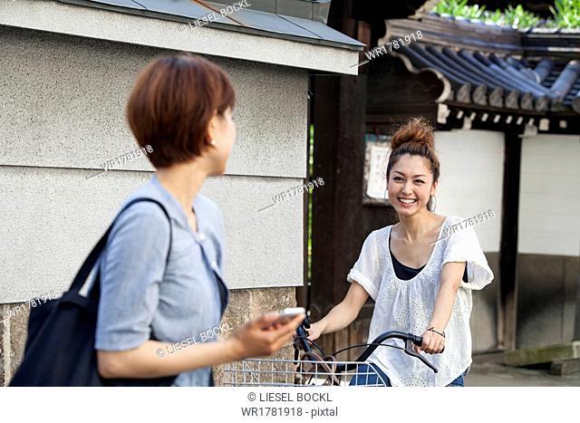 A woman chatting to another woman sitting on a bicycle