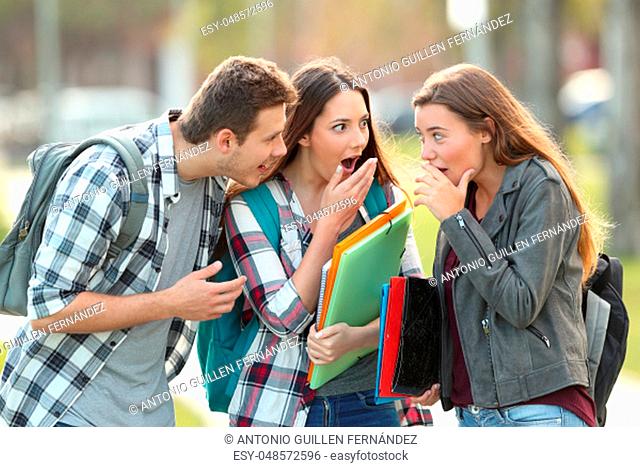 Three gossip students telling secrets in the street
