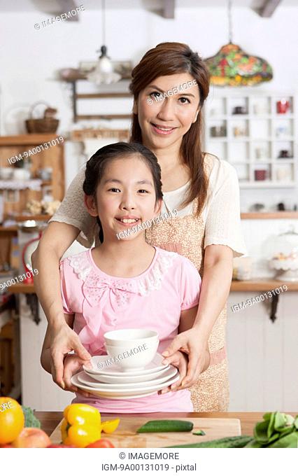 Mother and daughter holding a set of plates and bowls in kitchen
