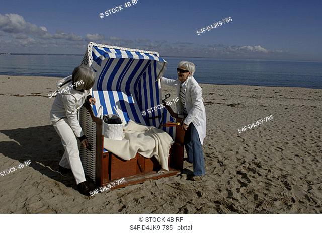 Two mature women adjusting a beach chair
