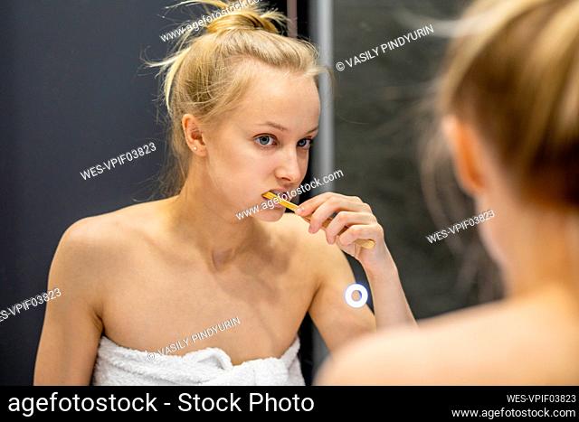 Reflection of woman on mirror brushing teeth in bathroom