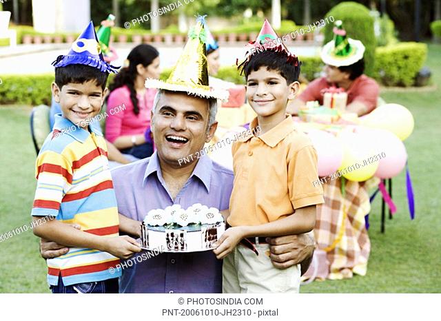 Two boys standing with their father and holding a birthday cake