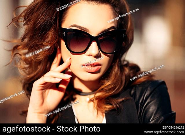 Gorgeous brunette woman with plump lips, sensuality touching face skin and posing at camera in windy weather. Beautiful girl in sunglasses