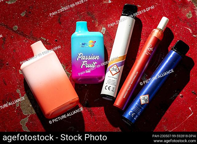 05 May 2023, Lower Saxony, Hanover: Several disposable e-cigarettes lie on a table. On the outside, they resemble colored felt-tip pens and come in fruity...