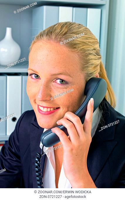 Eine freundliche Frau telefoniert an ihrem Schreibtisch im Büro und notiert Termine im Kalender