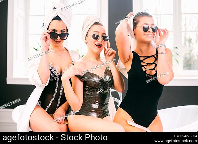 Theme female friendship. Party girlfriends, relaxation and spa procedures, hen party. Three Caucasian beautiful women sitting inside on bathroom in sunglasses