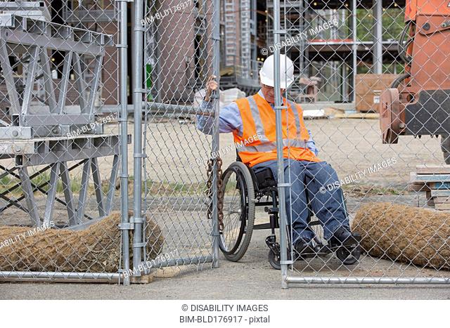 Caucasian engineer in wheelchair opening construction site gate
