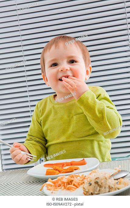 Baby boy feeding himself at dining table