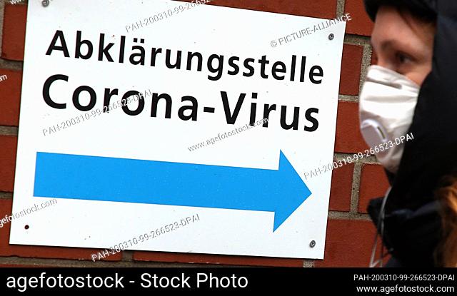 10 March 2020, Berlin: A young woman wearing a protective mask walks past a sign pointing to the Coronavirus clarification centre at the Vivantes Wenckebach...