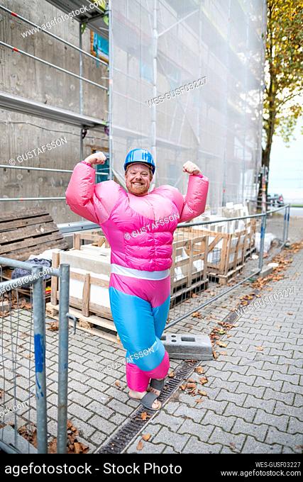 Portrait of a proud man wearing pink bodybuilder costume and hard hat at construction site