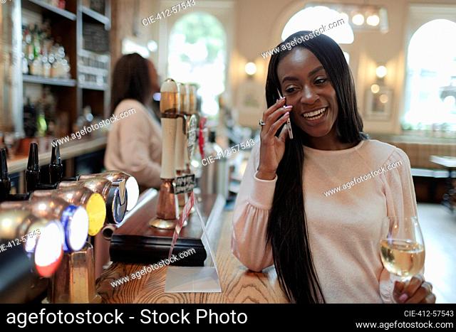 Young woman talking on smart phone and drinking wine in pub