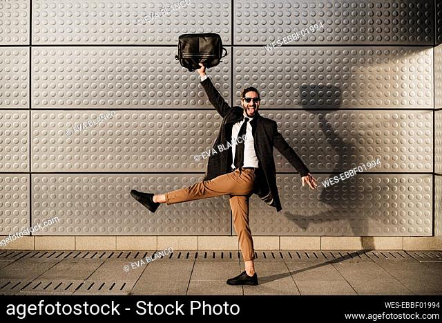 Carefree businessman holding briefcase while walking on footpath