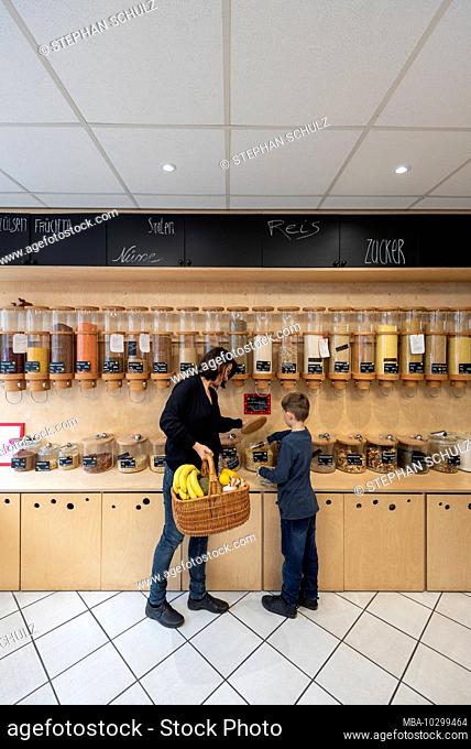 A woman and a boy are standing in front of a shelf with filling containers for grain in the packaging-free shop Frau Erna`s loser LebensMittelpunkt in Magdeburg