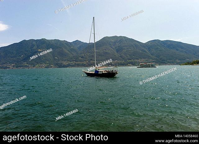 a boat on the water with some mountains in the back - lago di maggiore