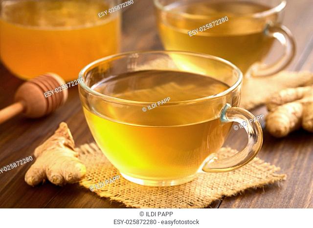 Hot ginger tea in glass cups with honey in the back, photographed on wood with natural light (Selective Focus, Focus on the front of the rim and the handle of...