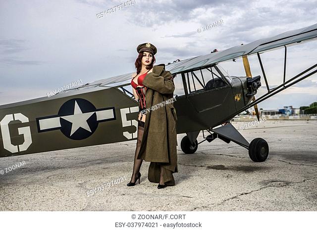 Plane, beautiful redhead pin up style wearing uniform wii with vintage aircraft war