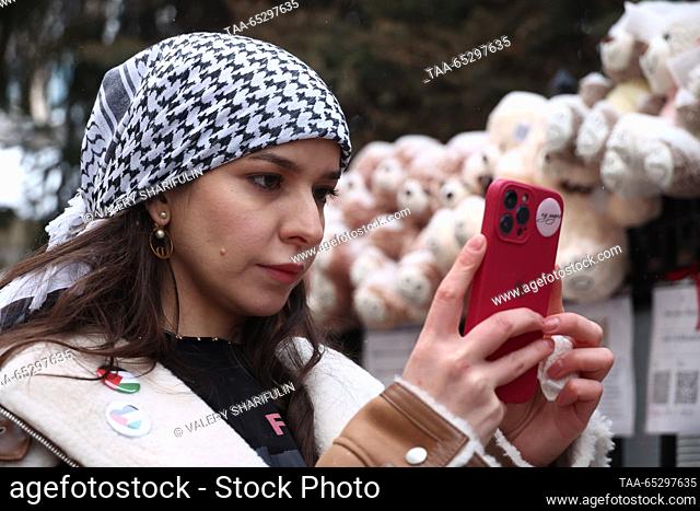 RUSSIA, MOSCOW - NOVEMBER 28, 2023: A woman wearing a Palestinian keffiyeh takes a photograph on her mobile phone outside the Palestinian Embassy on the...