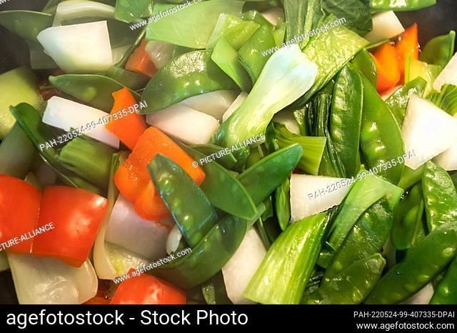23 May 2022, Baden-Wuerttemberg, Rottweil: Sugar snap peas, red bell peppers, kohlrabi and pak choi are cooked in a wok. Photo: Silas Stein/dpa