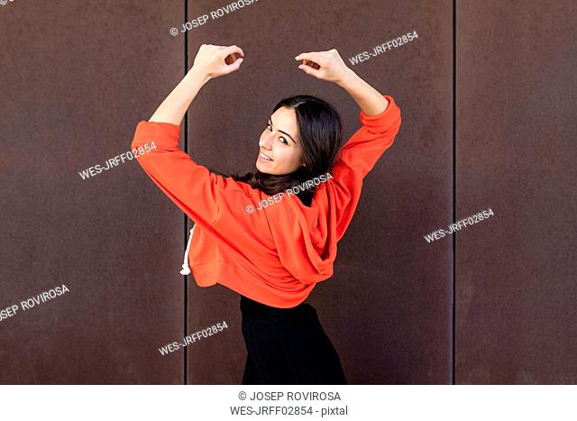 Young contemporary dancer in front of a rusty wall dancing and looking at camera